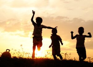 Silhouettes of children as they play against the setting sun.